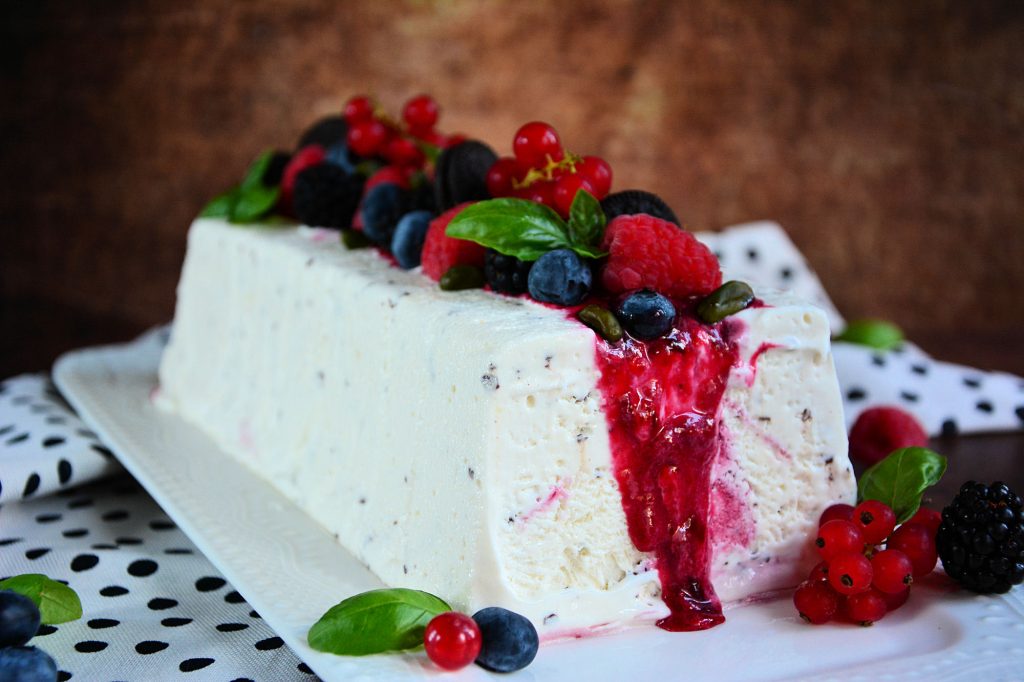 Stracciatella semifreddo sa voćnim prelivom i svežim malinama serviran na letnjem tanjiru